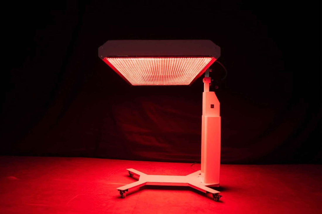 Een professioneel roodlicht LED-paneel op een witte standaard straalt intensief rood licht uit tegen een donkere achtergrond voor roodlichttherapie sessies